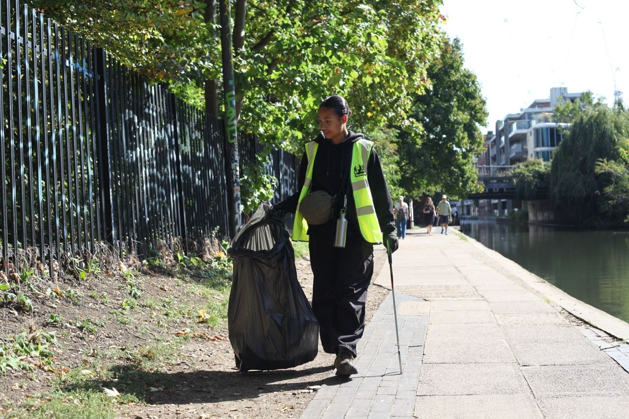 Person walking along the canal carrying litter picking equipment and wearing a hi vis